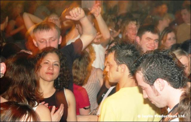 A packed crowd dancing, a person with a raised arm and another looking at the camera