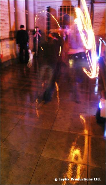 A blurred fire performer and a shiny floor, with two people standing in the background