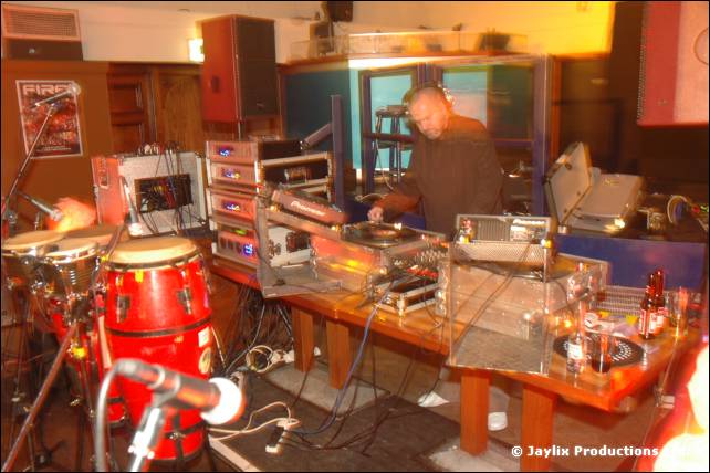 A DJ at turntables on a wooden table with a conga drum and a microphone in the foreground