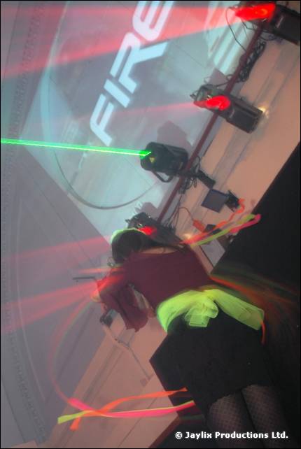 A dancer with a green waist wrap and ribbons in front of a projected FIRE logo and green laser
