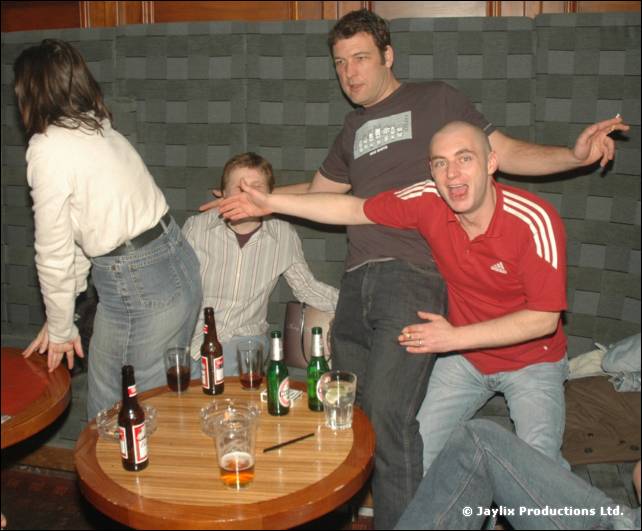 People dance and pose around a small table with bottles and glasses in a booth area