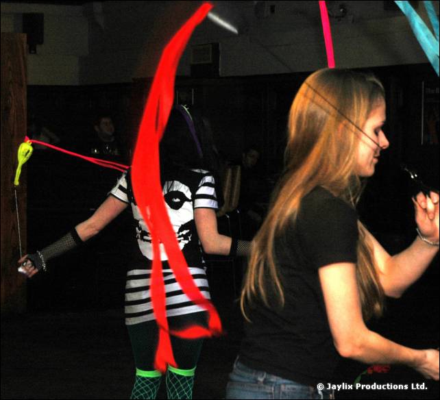 Two people dance with red ribbons on sticks, one in a striped top and one in a black t-shirt