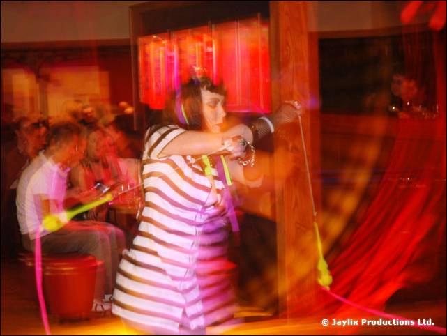 A person in a striped top swings a prop on a cord, motion blurred, with seated people behind