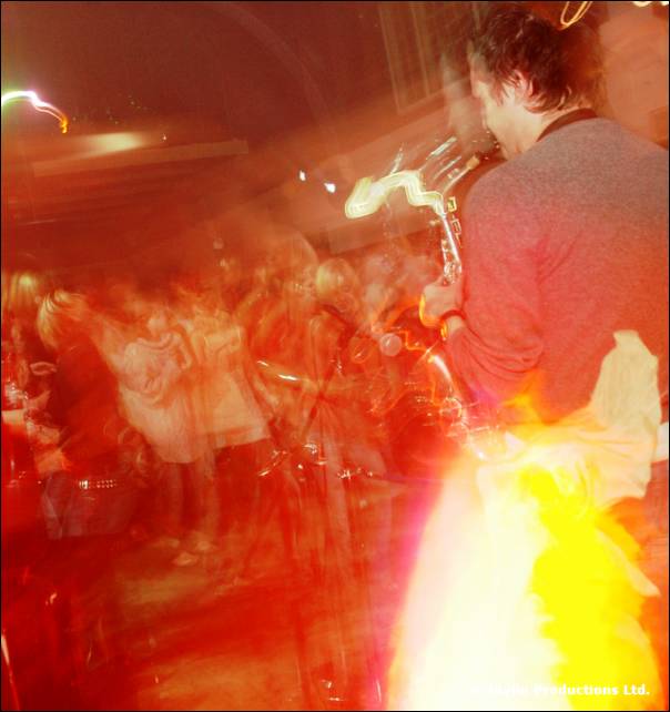A blurred crowd with a saxophonist at the right and bright orange flame below them