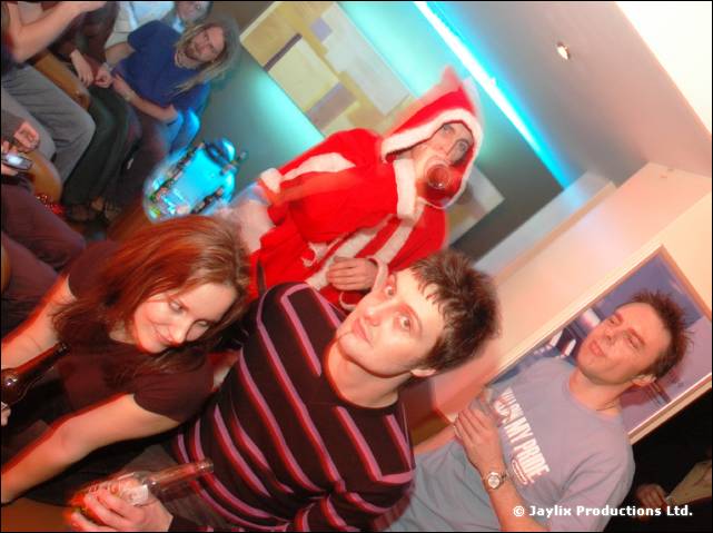 A group sit on sofas, one person in a Santa outfit leaning over the back