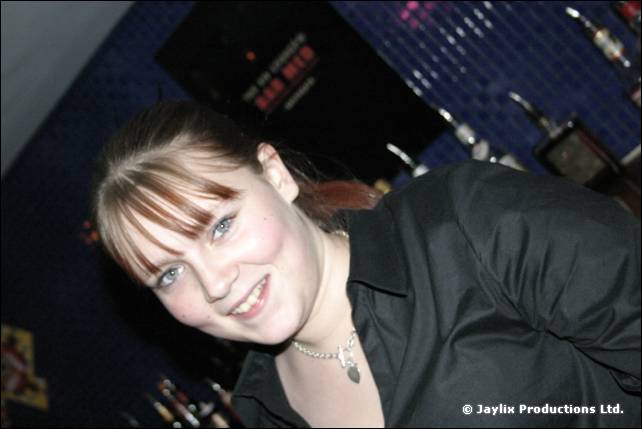 A smiling woman with a fringe and necklace leans towards the camera