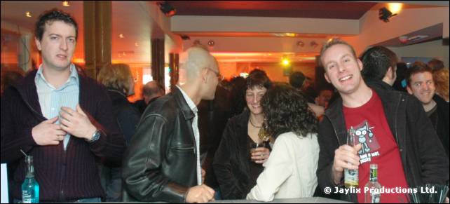 Several people stand at a bar, a man in a red T-shirt smiling on the right