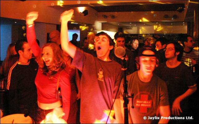 A crowd with raised arms at the front of a stage, people shouting and cheering