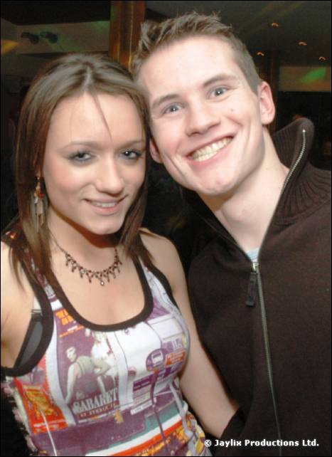 A young woman and a smiling young man in a dark jacket pose close together