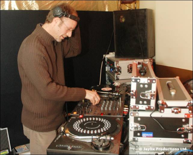 A DJ in a brown jumper and headphones mixes at turntables