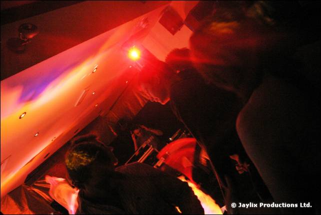 A dark, red-lit room with a bright spotlight and silhouetted people