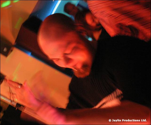A blurred bald man in dark clothes leans over, seen in orange and blue light
