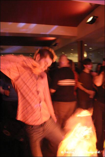 A man in a striped shirt dances in a dim bar with a glow at his feet