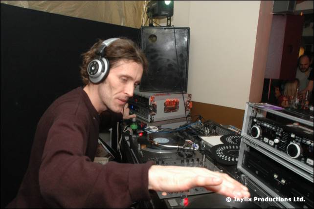 A DJ in a maroon top and headphones mixes at decks