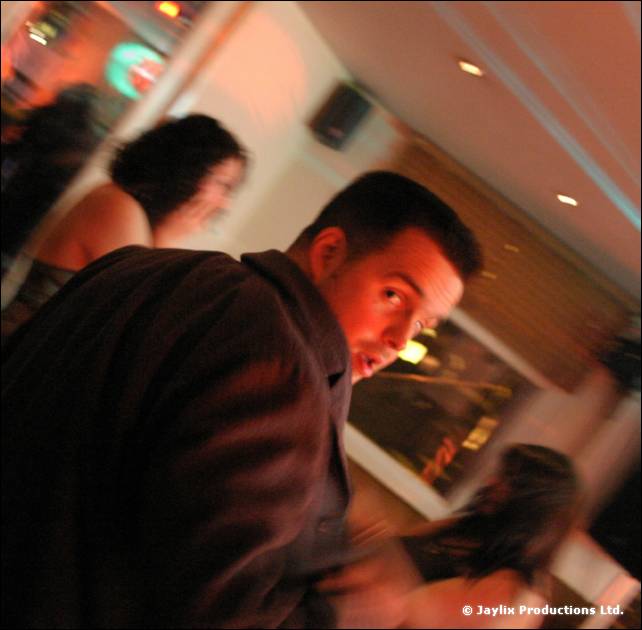 A man in a dark jacket looks over his shoulder in a bar, tilted view