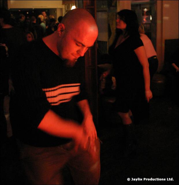 A bald man with a goatee in a black top looks down in a dark bar