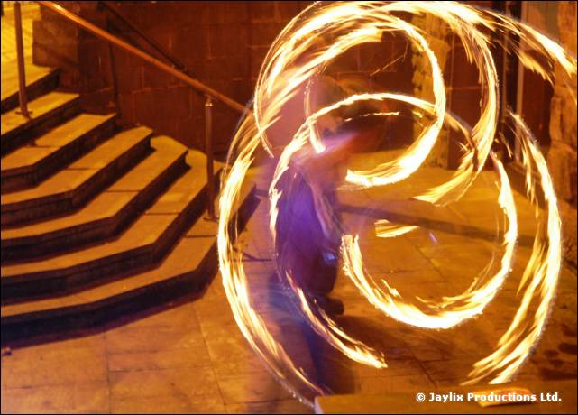 A person spins overlapping circles of fire beside a stone staircase at night