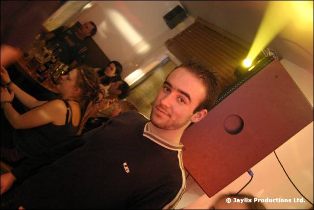 A man in a dark top smiles at the camera beside a speaker, tilted view