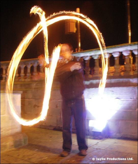 A person stands inside a large glowing ring of fire on a stone terrace at night