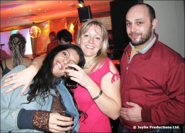 A woman in a pink top, a woman in a denim jacket and a bearded man in a red jacket pose together