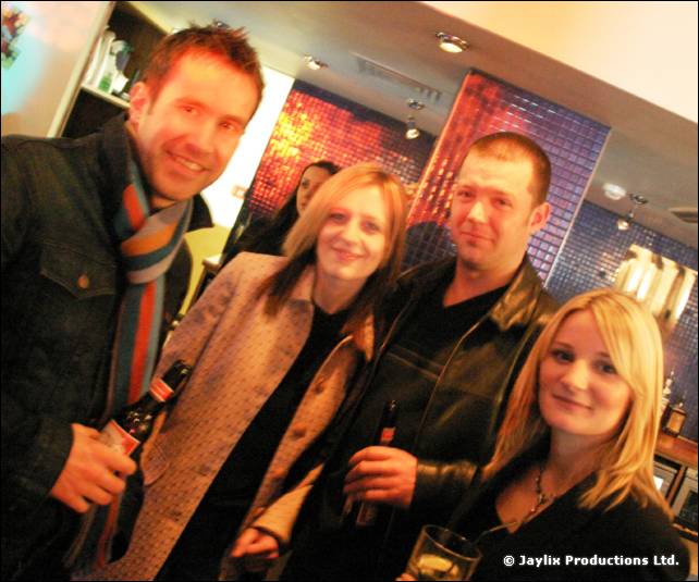 Two men and two women stand together in a bar holding drinks