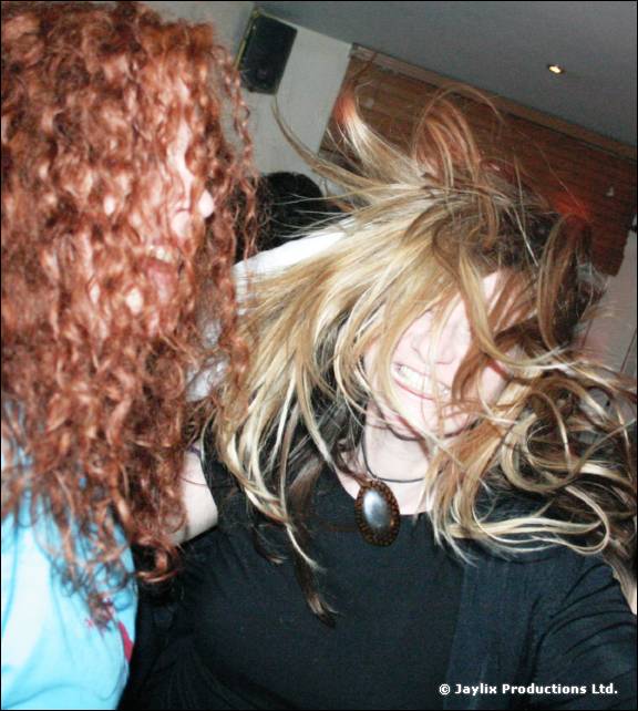 Two women dance closely, one with long curly red hair, the other with blonde hair flying