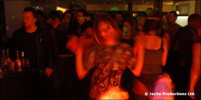 A blurred dancer in a patterned top on a red-lit dance floor with people behind