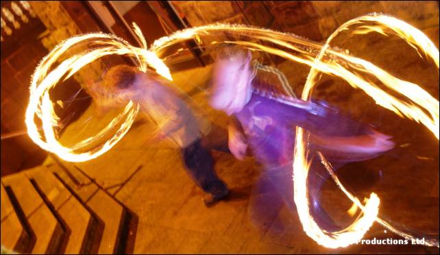 Two blurred figures stand on steps with looping trails of fire from spun poi around them