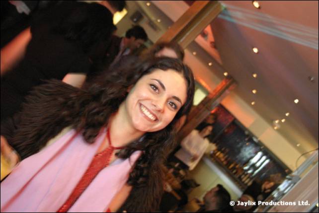 A smiling woman with long dark hair in a pink top poses in a busy bar