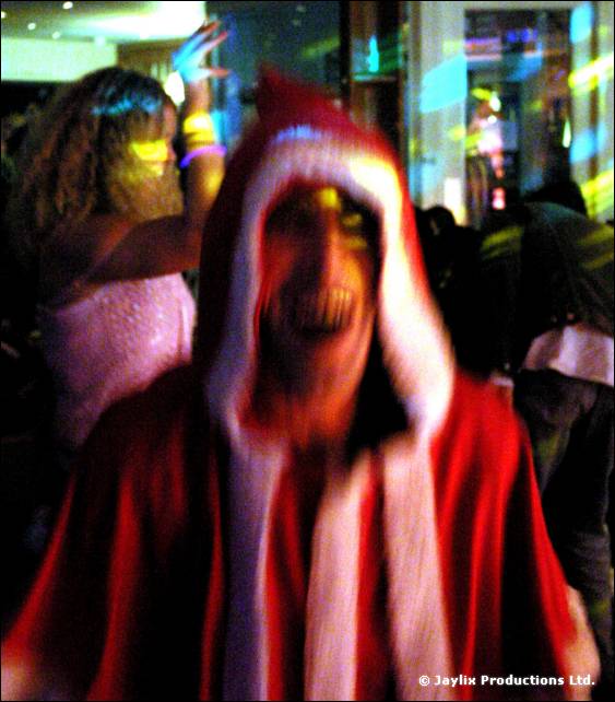 A person in a red and white hooded Father Christmas costume with a glowing face, blurred, in a club