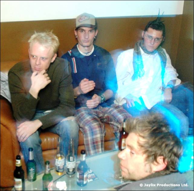 Three people sit on a leather sofa above a table of bottles, with a fourth person's head in the foreground