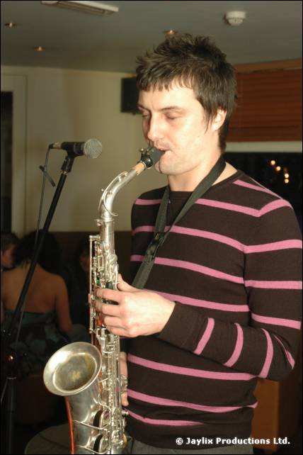 A man in a striped jumper plays a saxophone beside a microphone stand