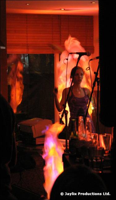A performer stands behind a microphone with tall flames rising from burners in front of them