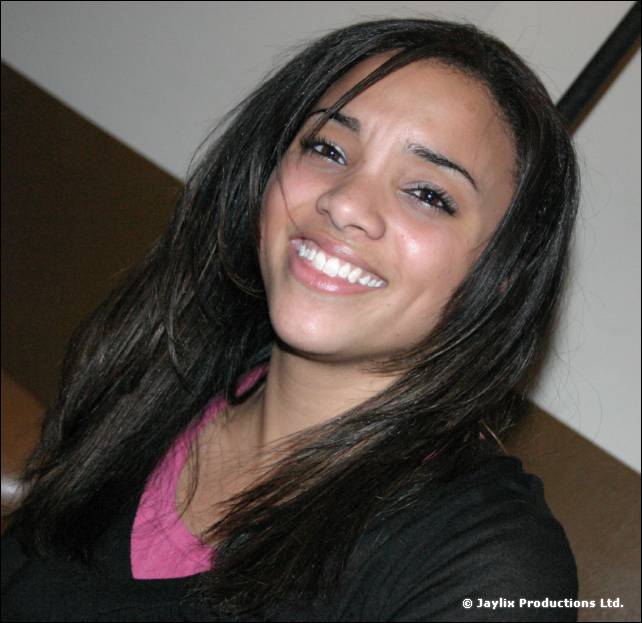 A smiling young woman with long dark hair and a pink top looks at the camera