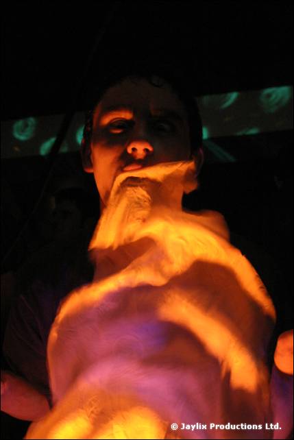 A dimly lit person holds a pale cloth or costume up to their chin in a dark club