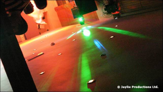 A dance floor seen from a low angle, lit by green and blue lasers and stage lights
