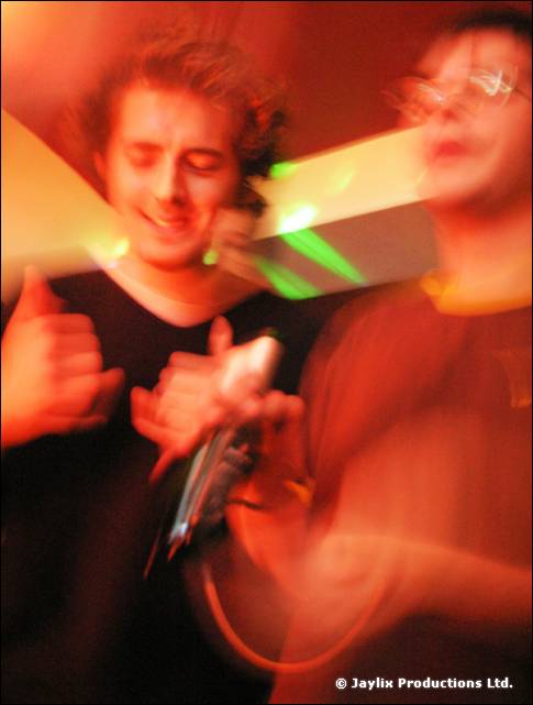 Two blurred people with a microphone between them, lit by green and orange lights