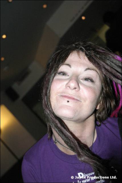 A woman with dark dreadlocks and a purple T-shirt smiles at the camera