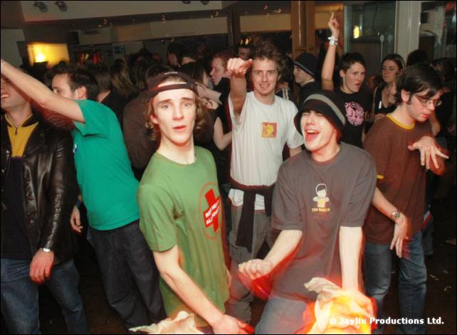 A crowded dance floor, young men in green and grey t-shirts with arms out
