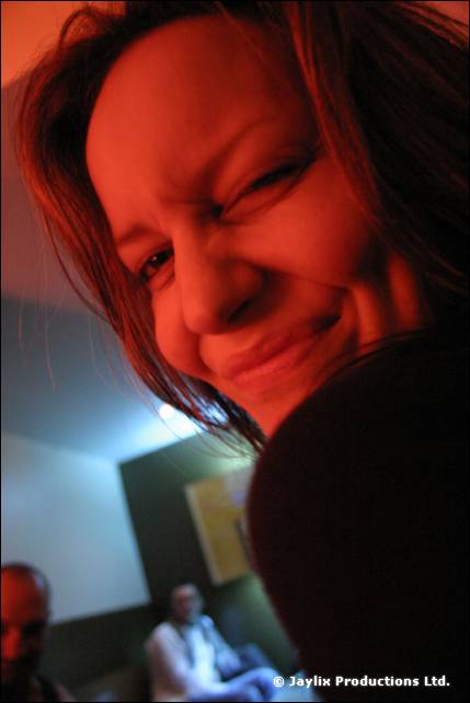A woman with long brown hair smiles and squints, with her face tilted close to the camera