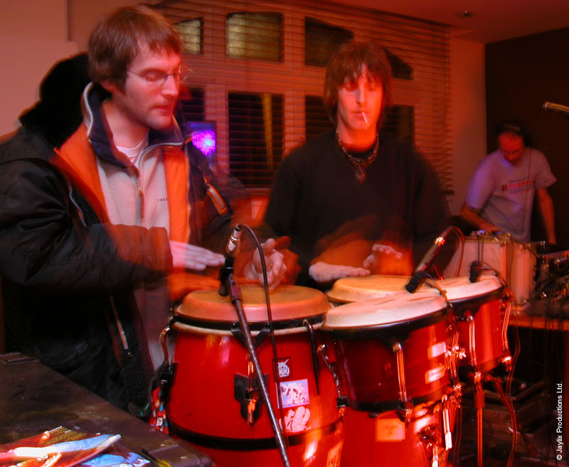 Two people play red congas with microphones in a dimly lit bar
