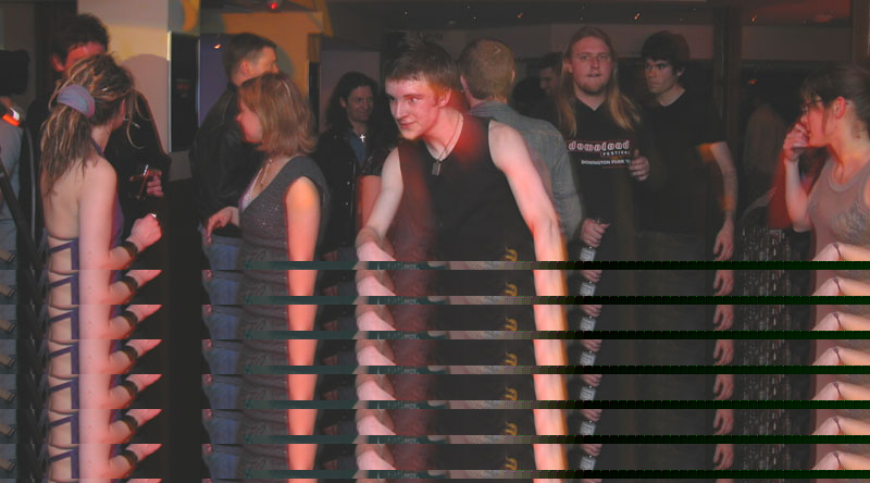 People dance in a dim bar, photographed through horizontal slats of a screen