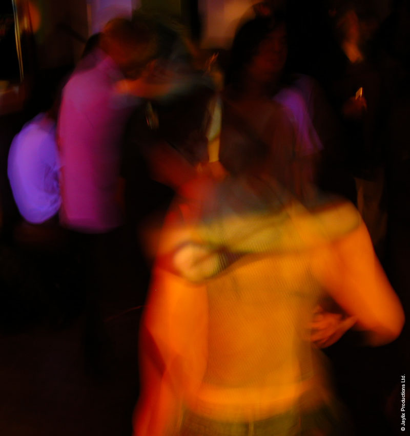 Heavily blurred dancers in purple, pink and orange light in a dark room
