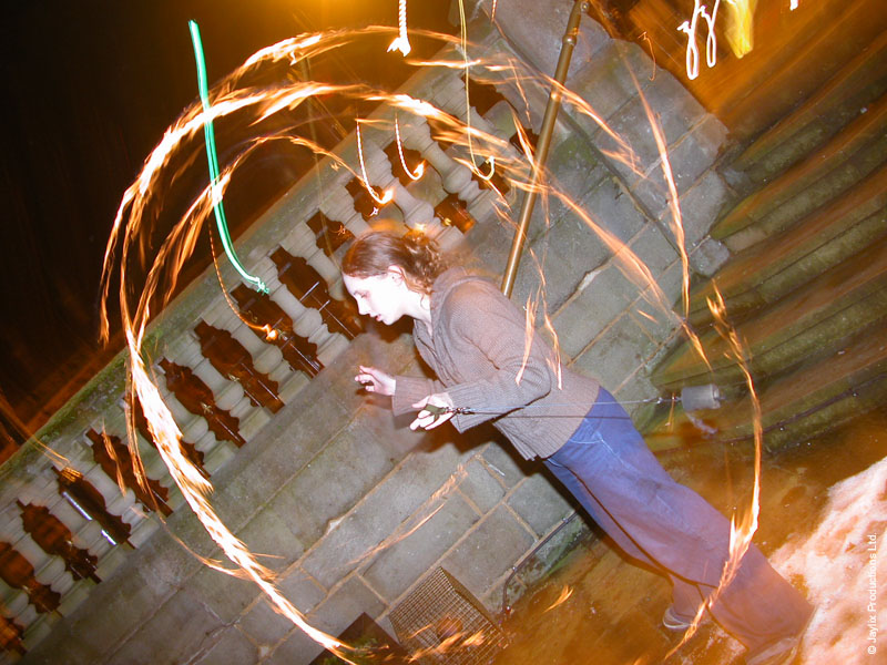 A person spins fire poi on stone steps at night, leaving bright circular light trails