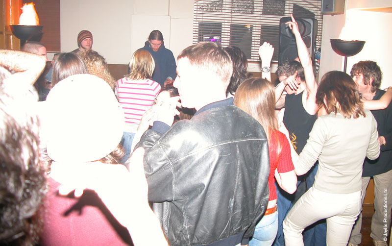 A crowd dances in a bar, with a flaming torch on a stand at the far wall