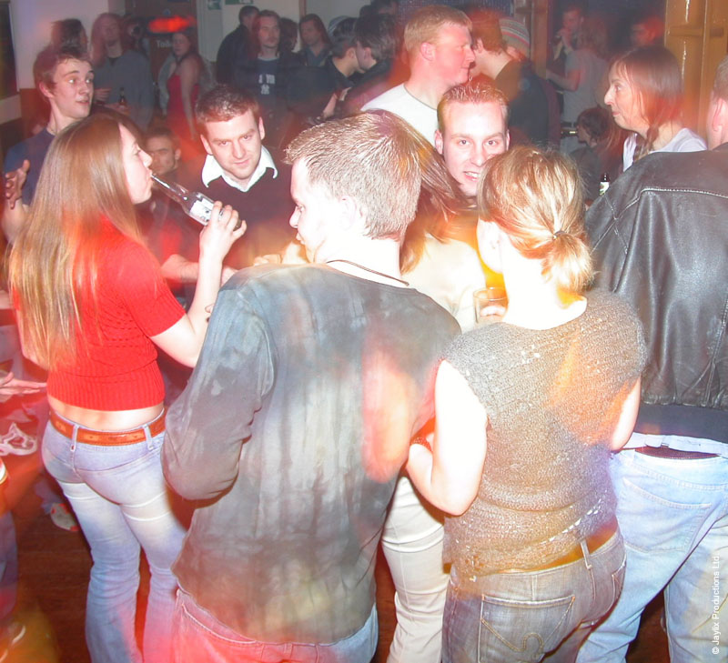 A crowded dance floor seen from behind with people in red and sparkly tops and blurred coloured lights