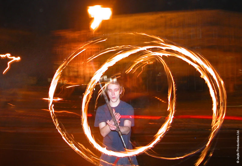 A person holds a staff inside two large circles of fire at night
