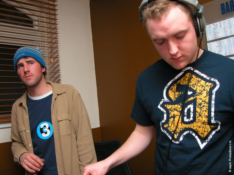 A person in a blue striped beanie and a DJ wearing headphones and a dark t-shirt stand beside a Bar Med sign