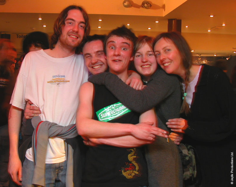 Five people hug and pose together in a bar, one in a black top reading Superbock