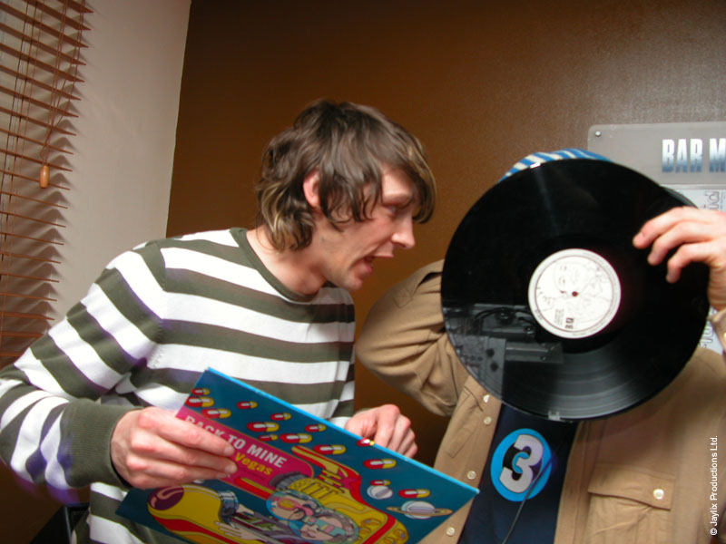 A person in a striped top looks at a record sleeve while another holds a vinyl record in front of their face